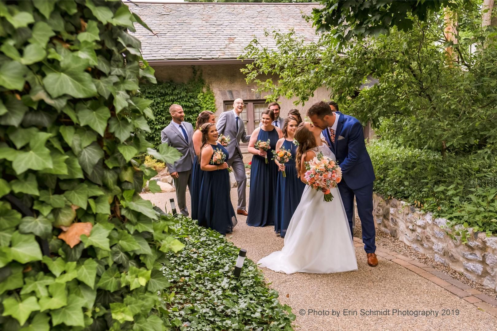 A bride and groom are kissing in front of their wedding party.