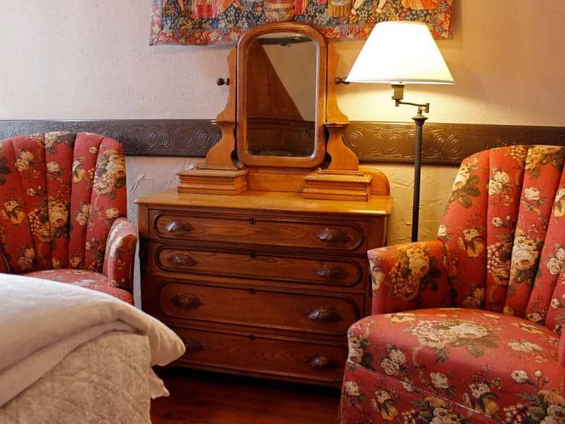 A bedroom with two chairs a dresser and a lamp