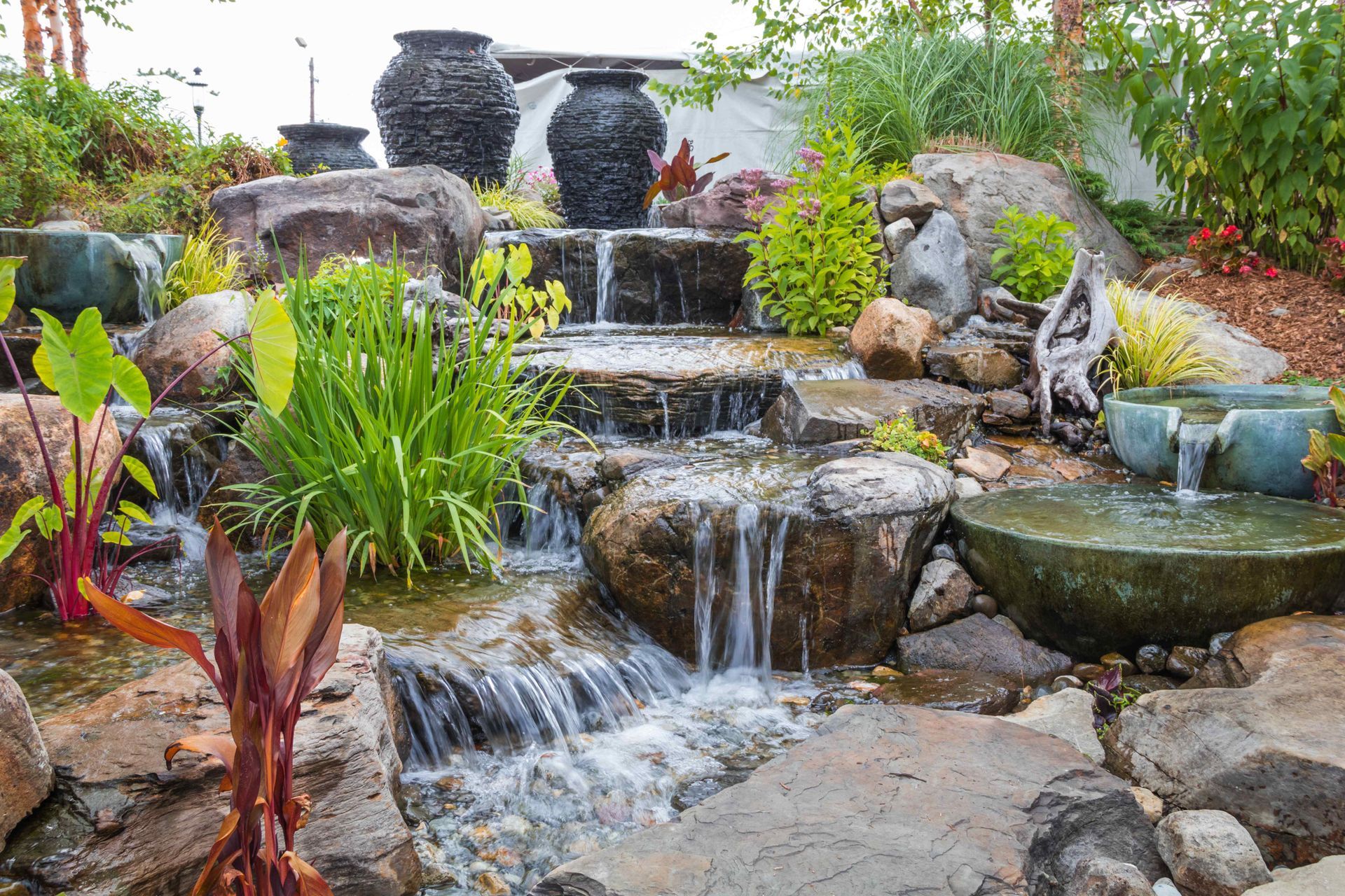 A waterfall is surrounded by rocks and plants in a garden.