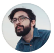 Man with a beard and glasses looks up and to the left, wearing a blue denim shirt, set against a white background.