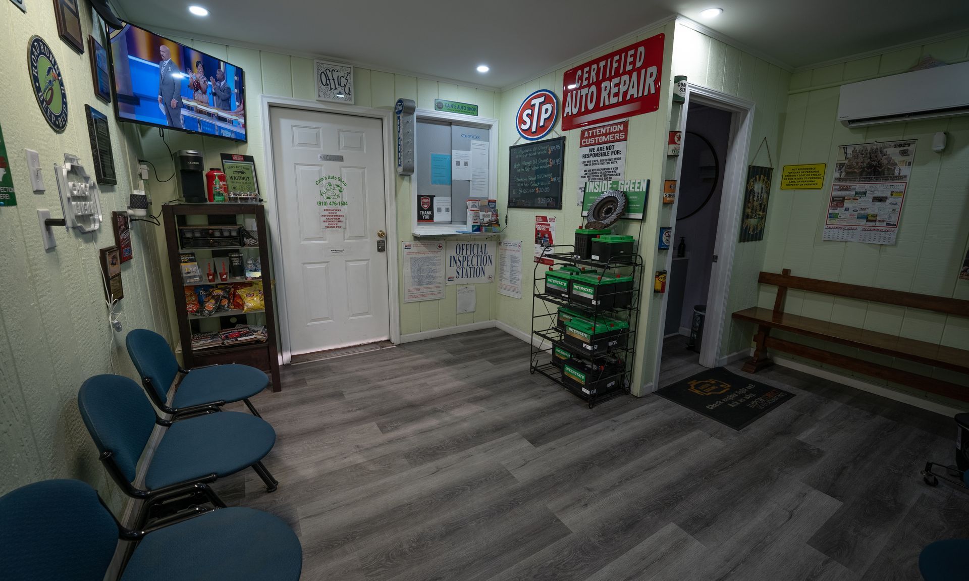 Waiting area of an auto repair shop with chairs, TV, signage, and a row of batteries. | Cain's Auto Shop