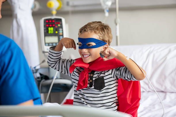 A young boy is wearing a superhero costume in a hospital bed.