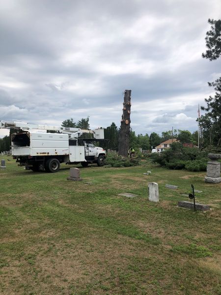 A white truck with a crane on top of it is parked in a cemetery.