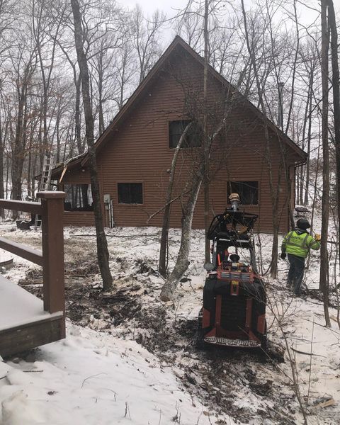 A man is driving a tractor in front of a house in the woods.