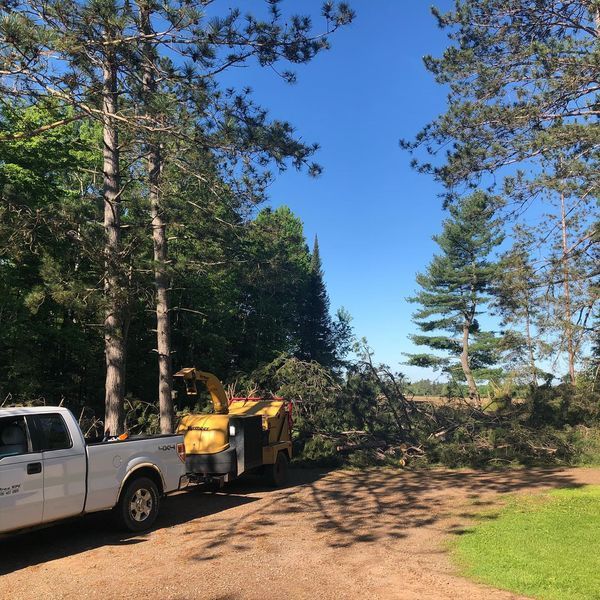 A white truck is parked on a dirt road next to a tree chipper.