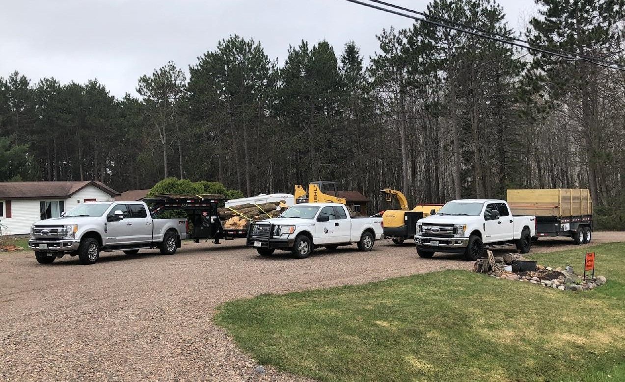 A row of trucks are parked in a gravel driveway in front of a house.