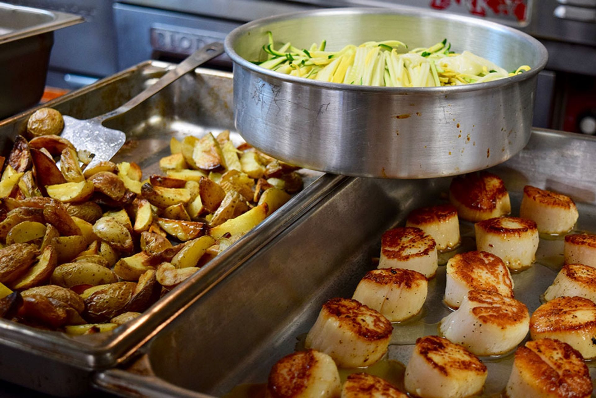 A pan of scallops next to a pan of potatoes.