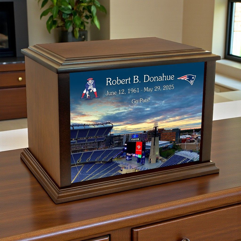 A wooden cremation urn featuring a photo of Gillette Stadium, New England Patriots logos, and a memorial inscription.
