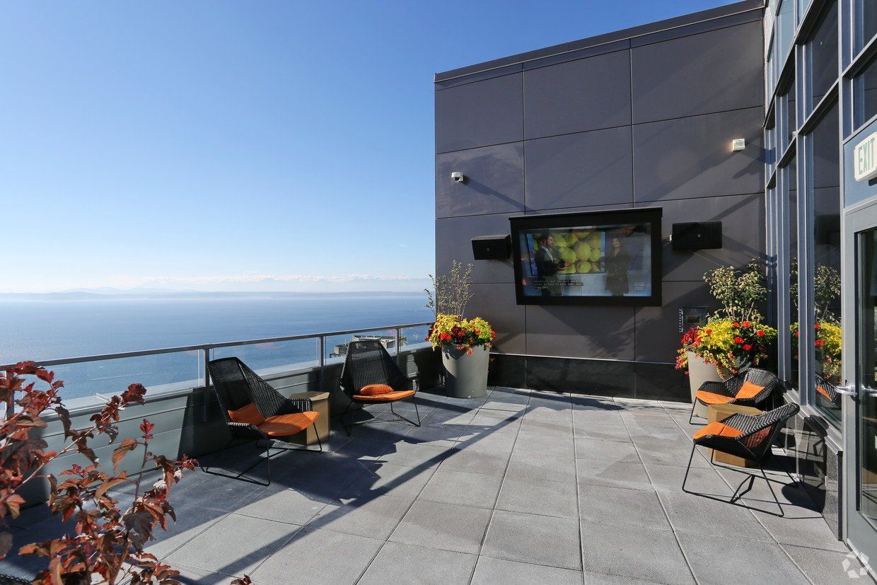 A balcony with chairs and a television on the wall overlooking the ocean.