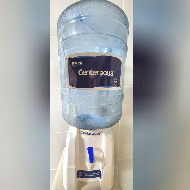 Gran jarra de agua azul sobre un dispensador blanco con la etiqueta Canderagua en un entorno interior luminoso.