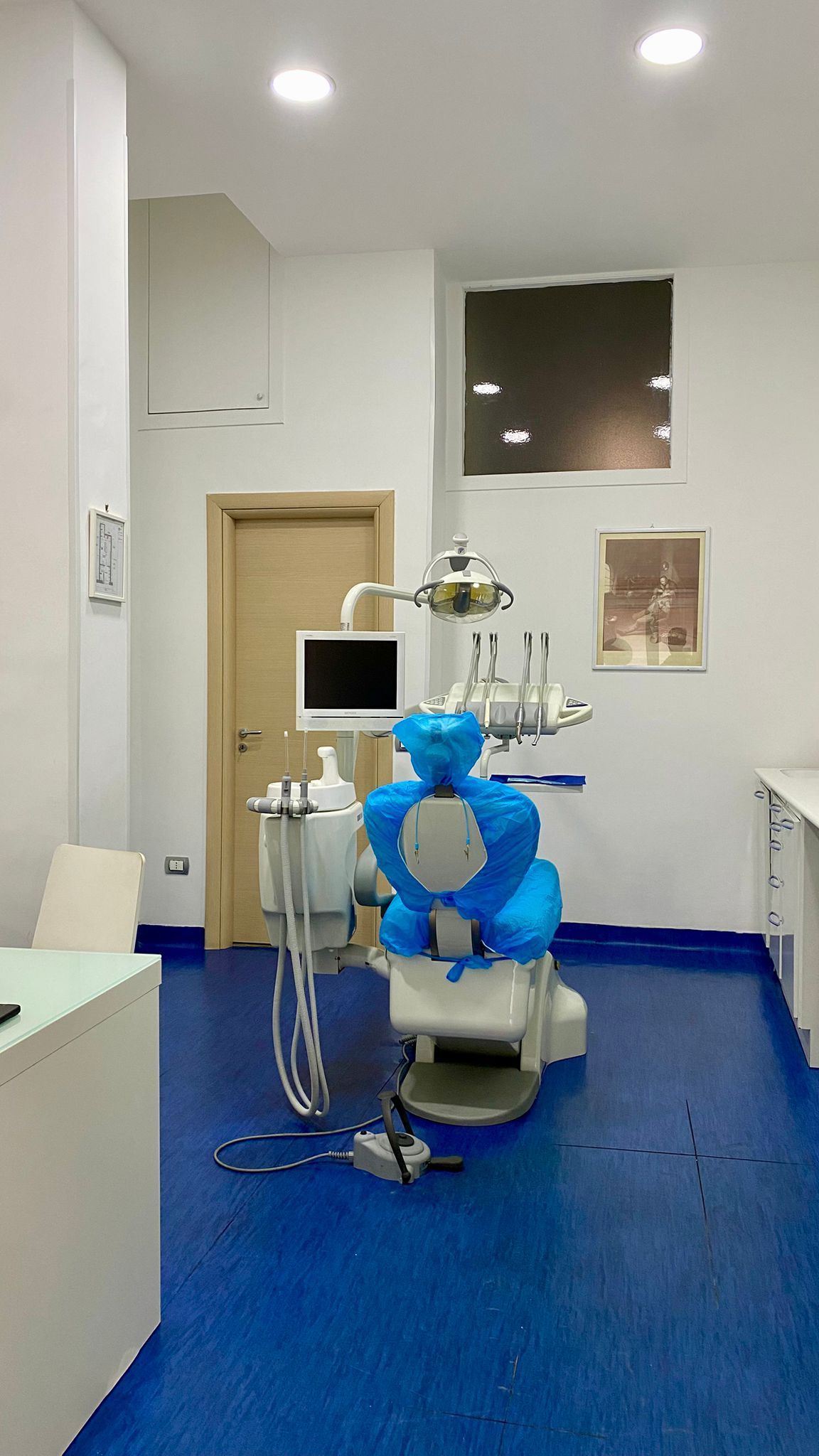 Interno di uno studio dentistico con pavimento blu, poltrona odontoiatrica ricoperta da un orso blu, attrezzatura.