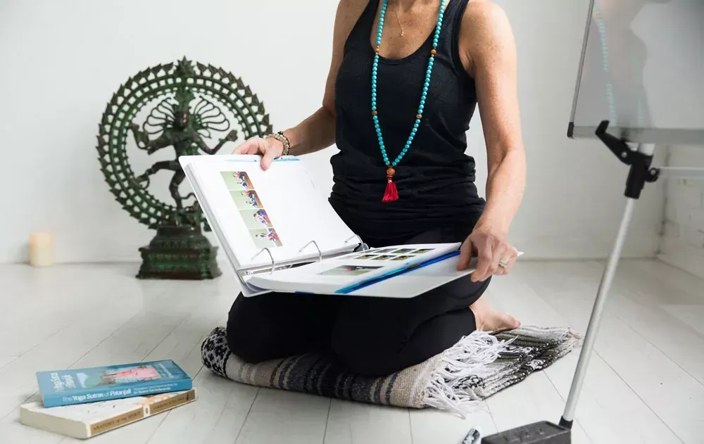 Woman studying a binder manual for a 200-hour yoga teacher training certification at Uptown Yoga .
