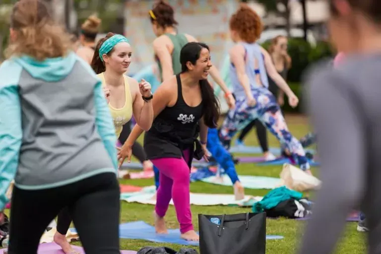 Smiling women participating in outdoor community Seva Yoga practice on the grass with Uptown Yoga.