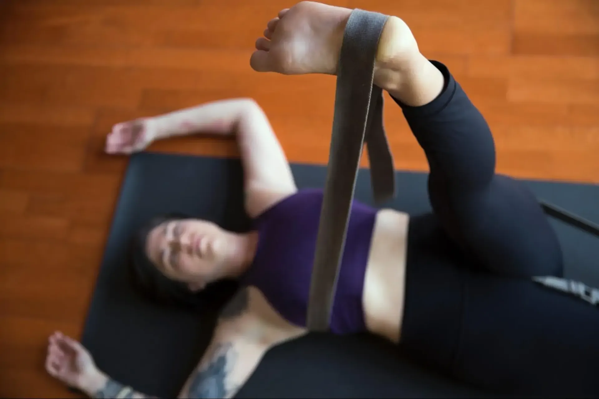 Close-up of a person using a yoga strap for a reclined hamstring stretch on a yoga mat.