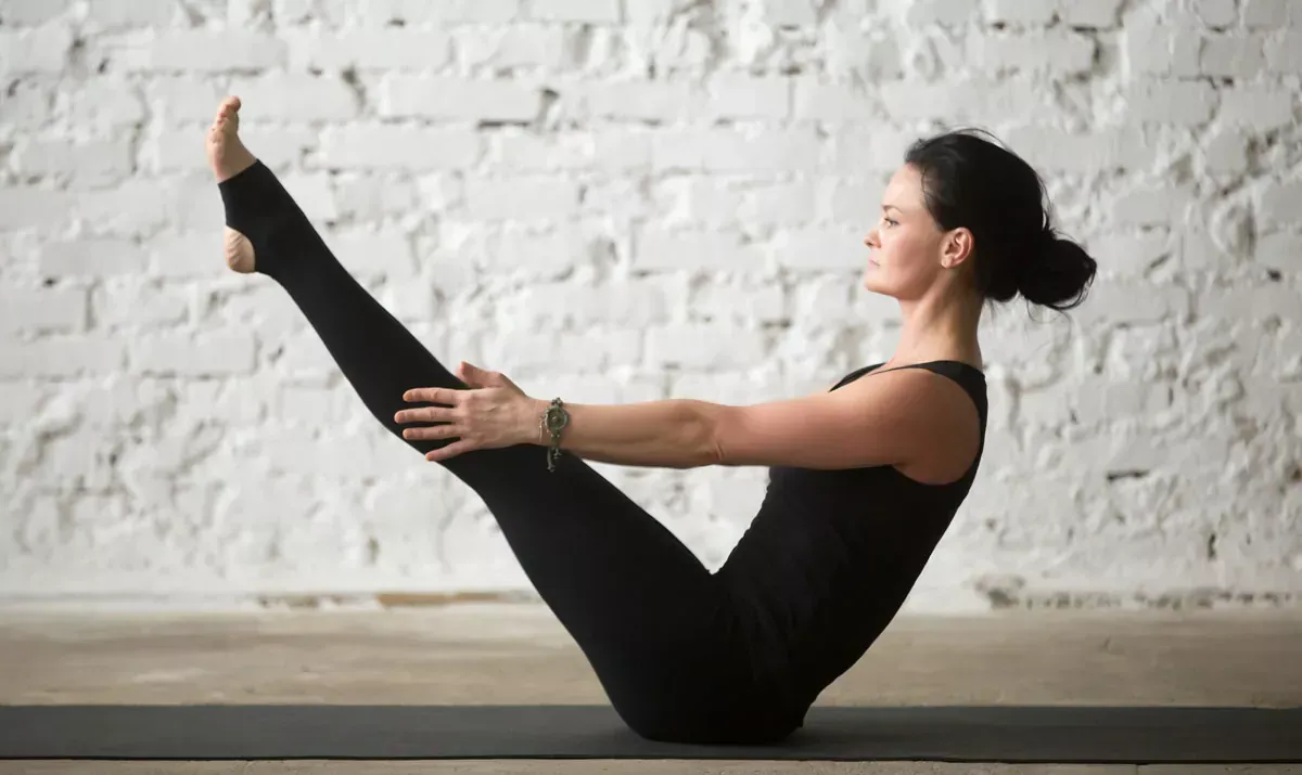 Woman demonstrating the Navasana boat pose in a studio to improve balance and abdominal strength.