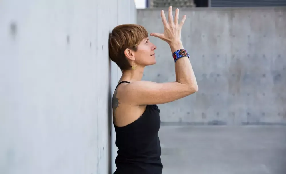 A woman sitting in reverse prayer yoga pose facing a large gong, representing heart chakra opening a