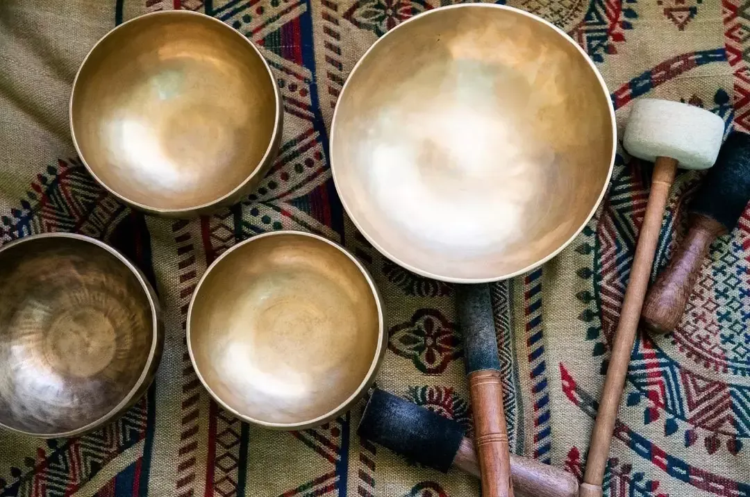 Four brass singing bowls and wooden mallets on a patterned cloth for sound healing at Uptown Yoga.