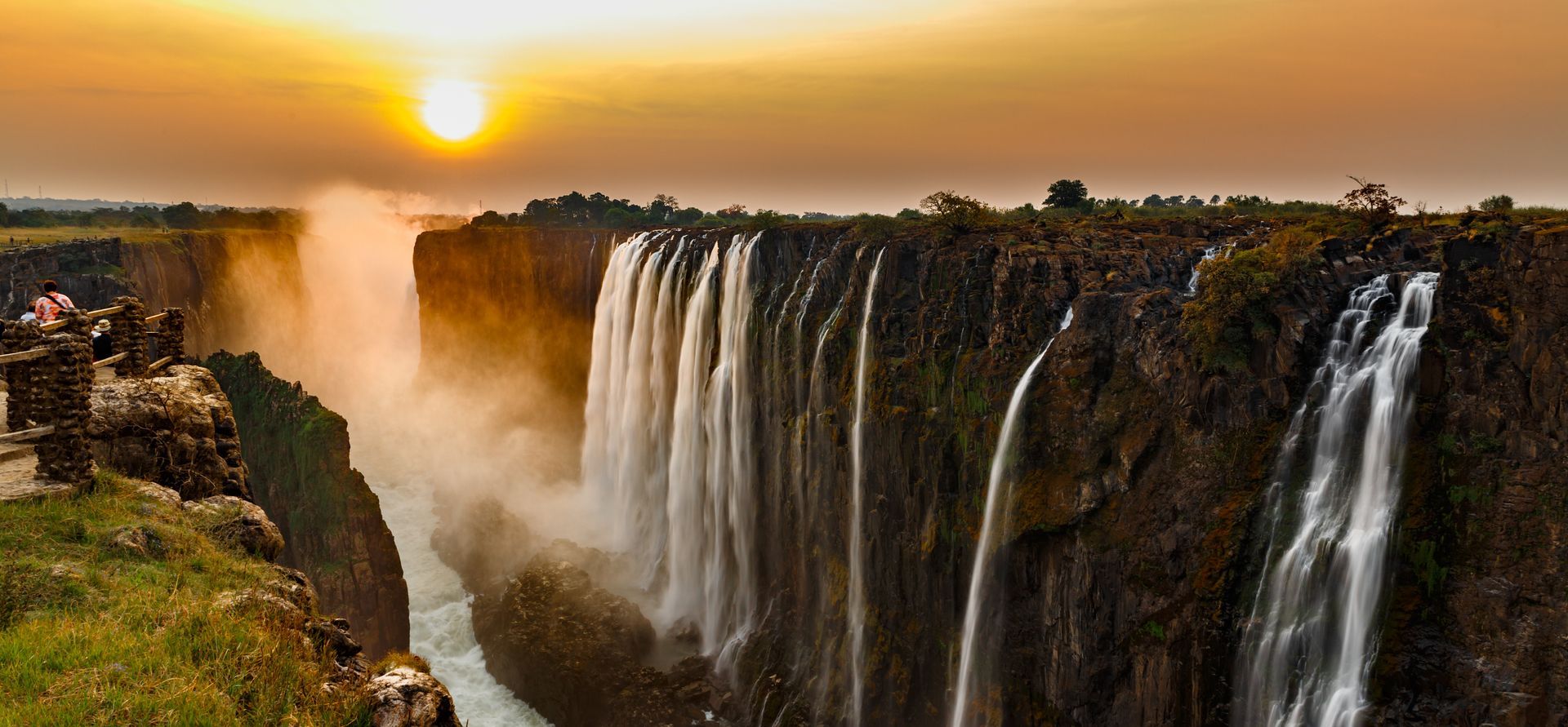 Golden sunset over Victoria Falls with mist rising from the cascading waterfalls in Zimbabwe.