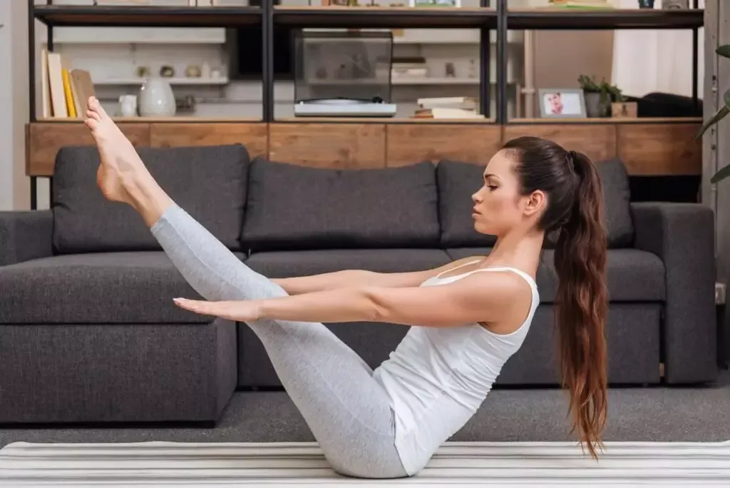 A woman practices a knee-to-chest plank pose variation on her yoga mat to build core strength.