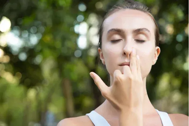 A woman practices alternate nostril breathing outdoors to calm her mind, reduce stress, and balance 