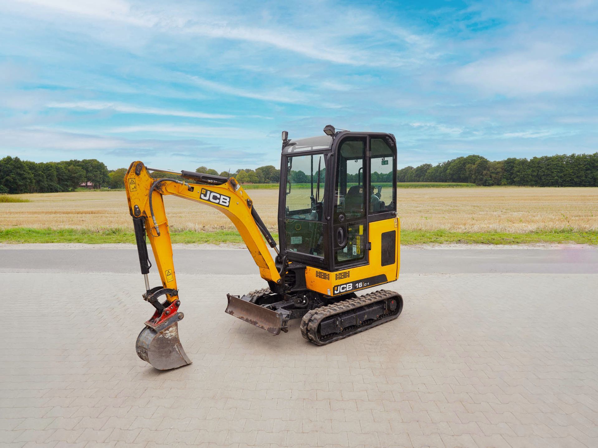 Gelb-schwarzer JCB-Minibagger auf einer gepflasterten Fläche.
