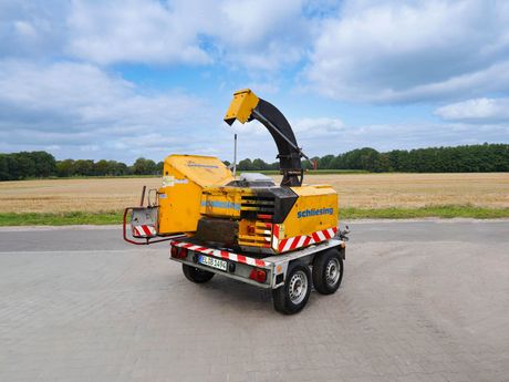 Gelber Holzhäcksler auf einem Anhänger, im Freien an einer Straße geparkt, einsatzbereit.