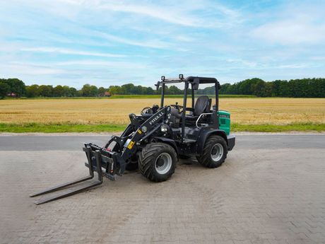 Kompaktradlader von Pritbull in grün und schwarz steht auf einer gepflasterten Fläche.