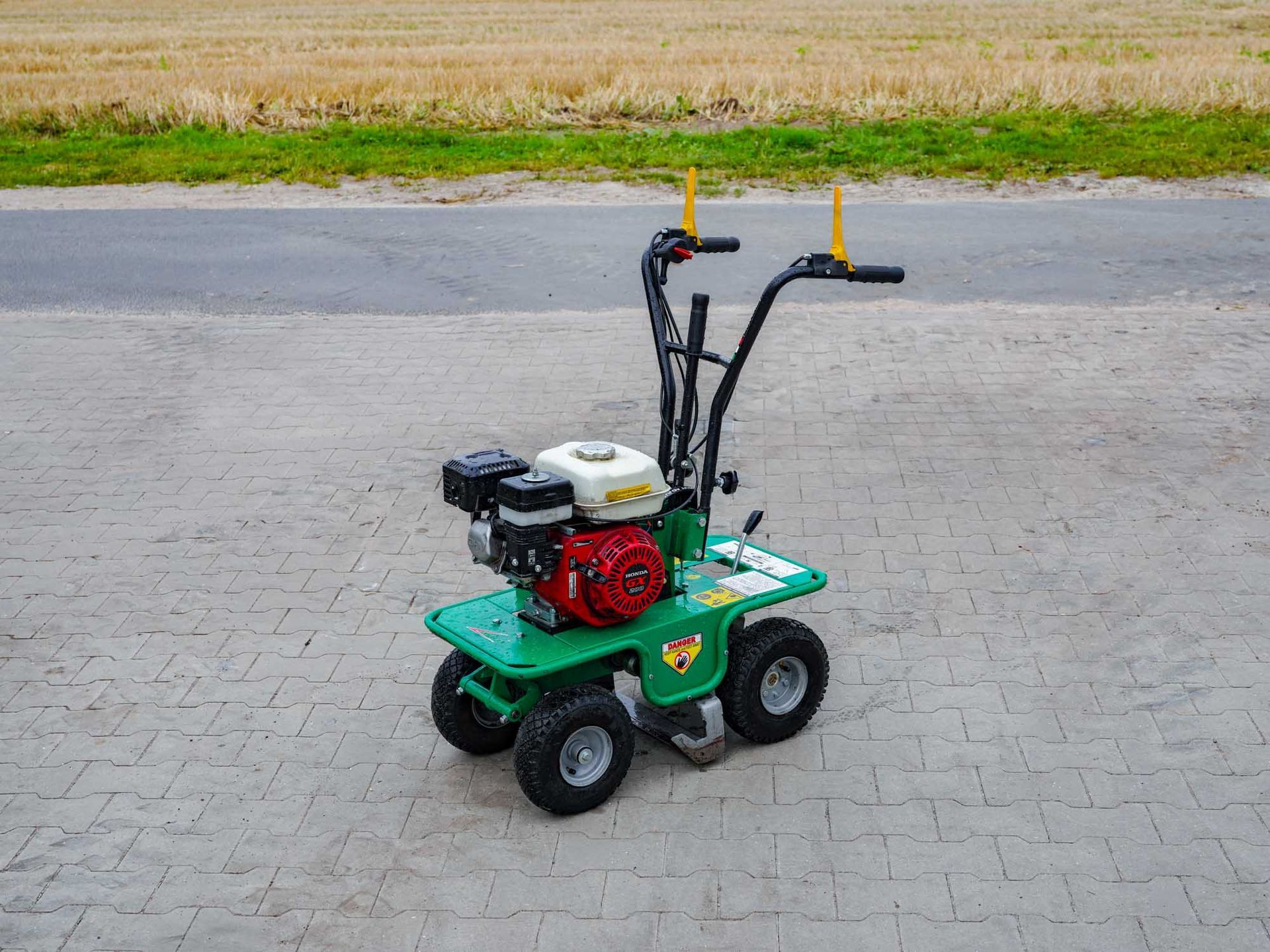 Grün-rote vierrädriger Sonderschneider mit kleinem Motor, auf Pflastersteinen geparkt.