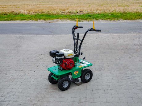 Grün-rote vierrädriger Sonderschneider mit kleinem Motor, auf Pflastersteinen geparkt.