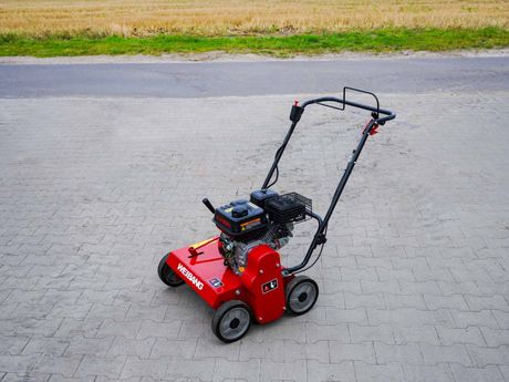 Rote Benzin Vertikutierer auf grau gepflasterter Fläche, im Hintergrund ein Feld.