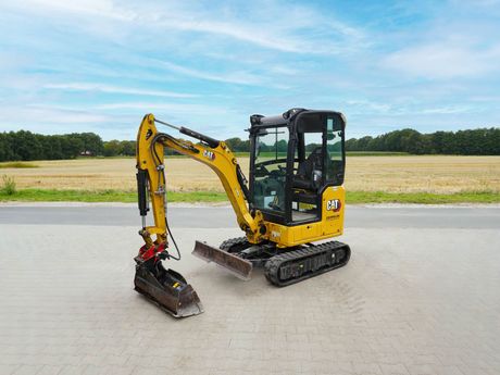 Gelb-schwarzer CAT-Minibagger auf einer gepflasterten Fläche.