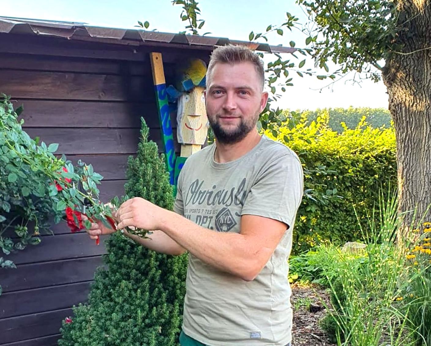 Mann schneidet Rosen im Garten. Er trägt ein grünes Hemd und lächelt.