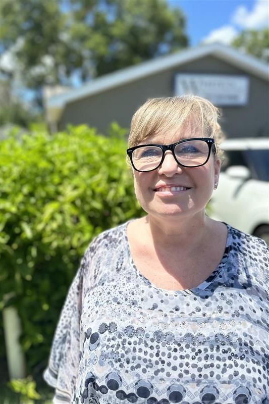 A woman wearing glasses and a blue shirt is smiling for the camera.