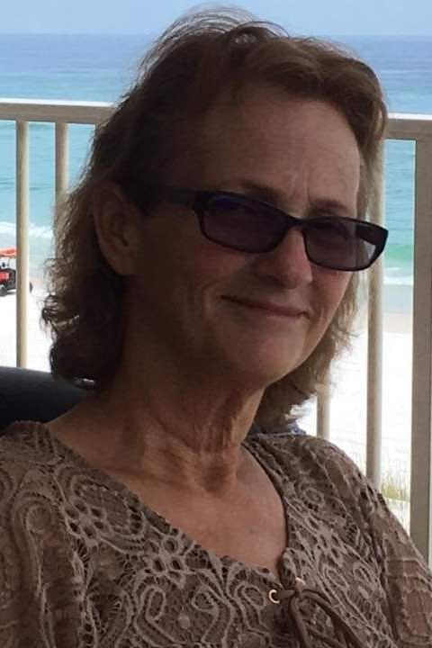 A woman wearing sunglasses is sitting on a balcony overlooking the ocean.