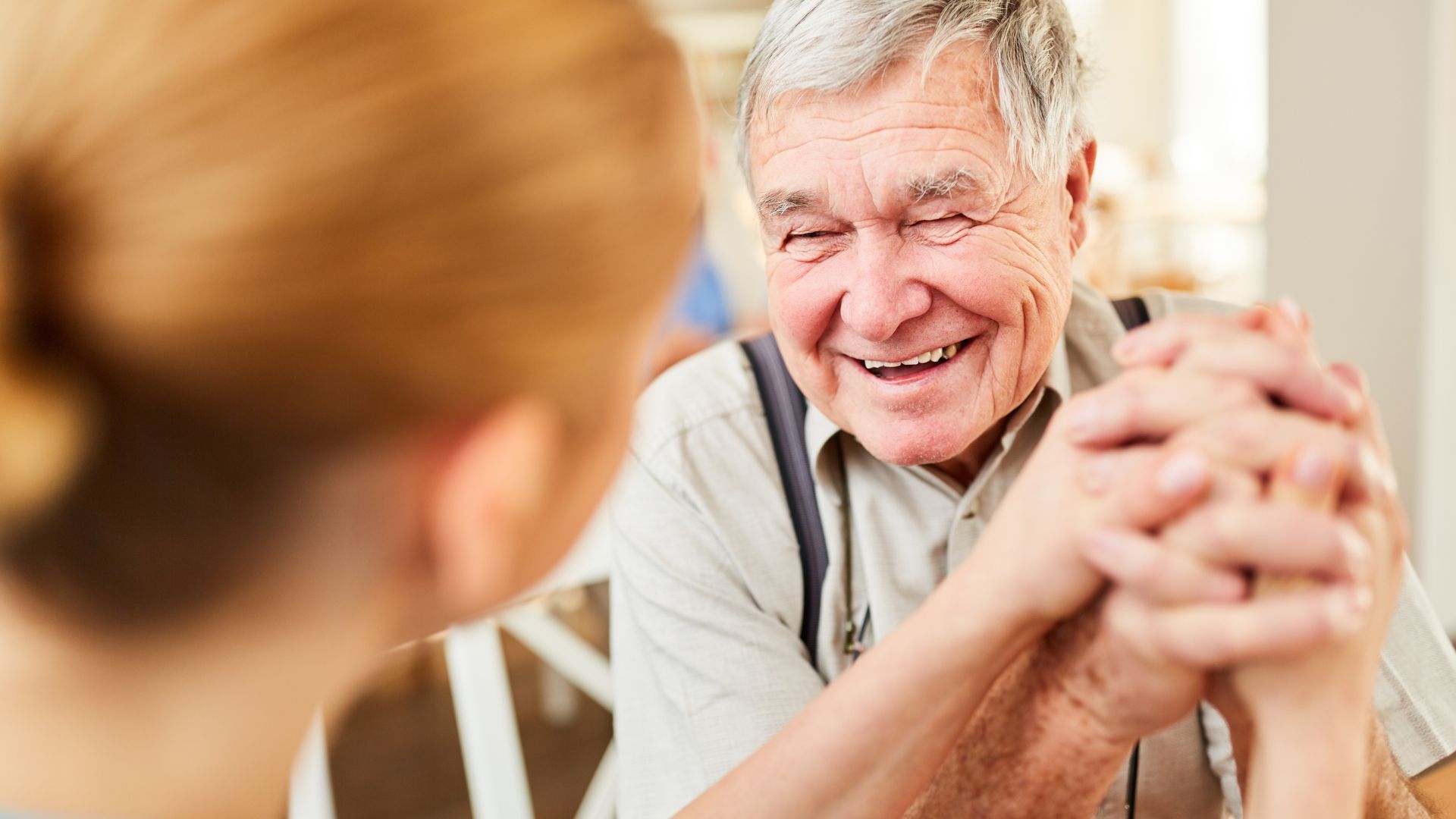 An elderly man is holding a woman's hand and smiling.