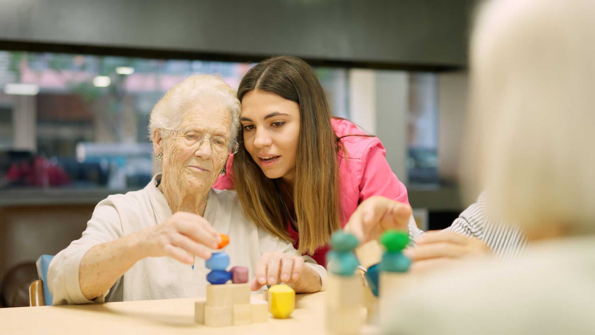 A woman is helping an elderly woman build a pyramid with wooden blocks.