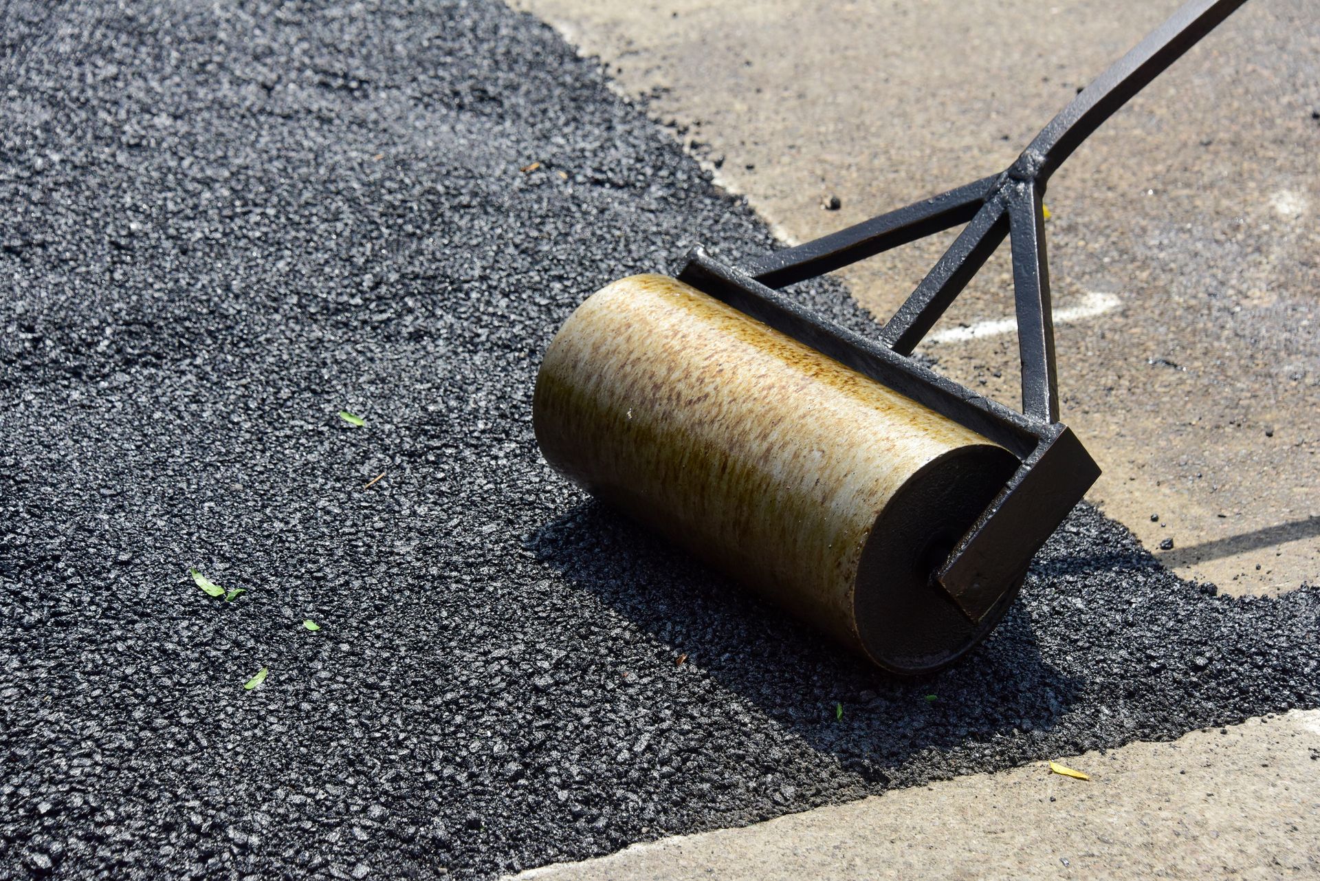 Close-up image of a steamroller smoothing out freshly laid asphalt on a road.