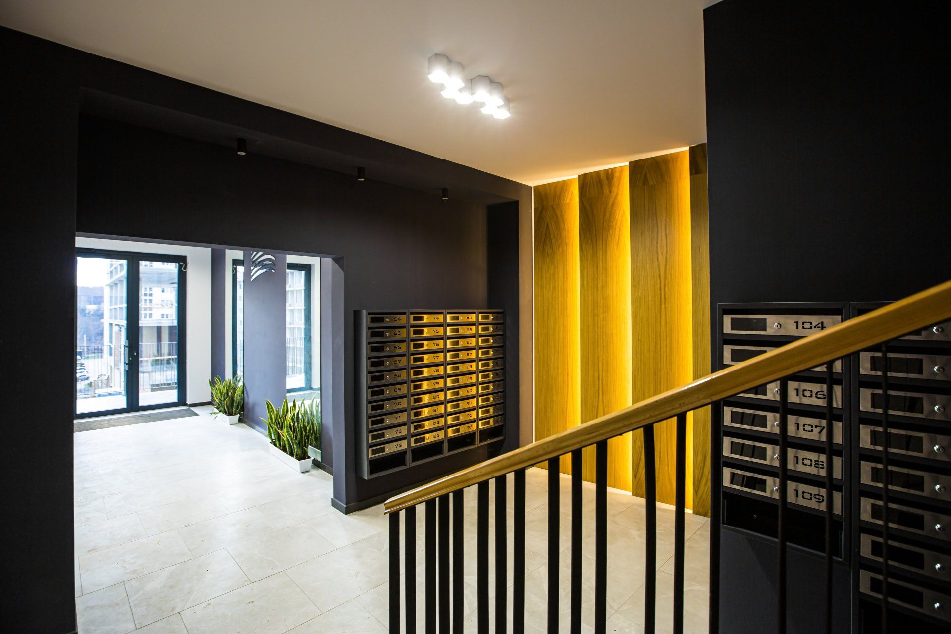 Apartment building lobby with mailboxes, black walls, gold accents, and a staircase.