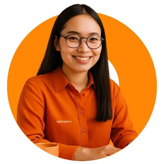 Woman with glasses smiling, wearing orange shirt, in front of orange circle.