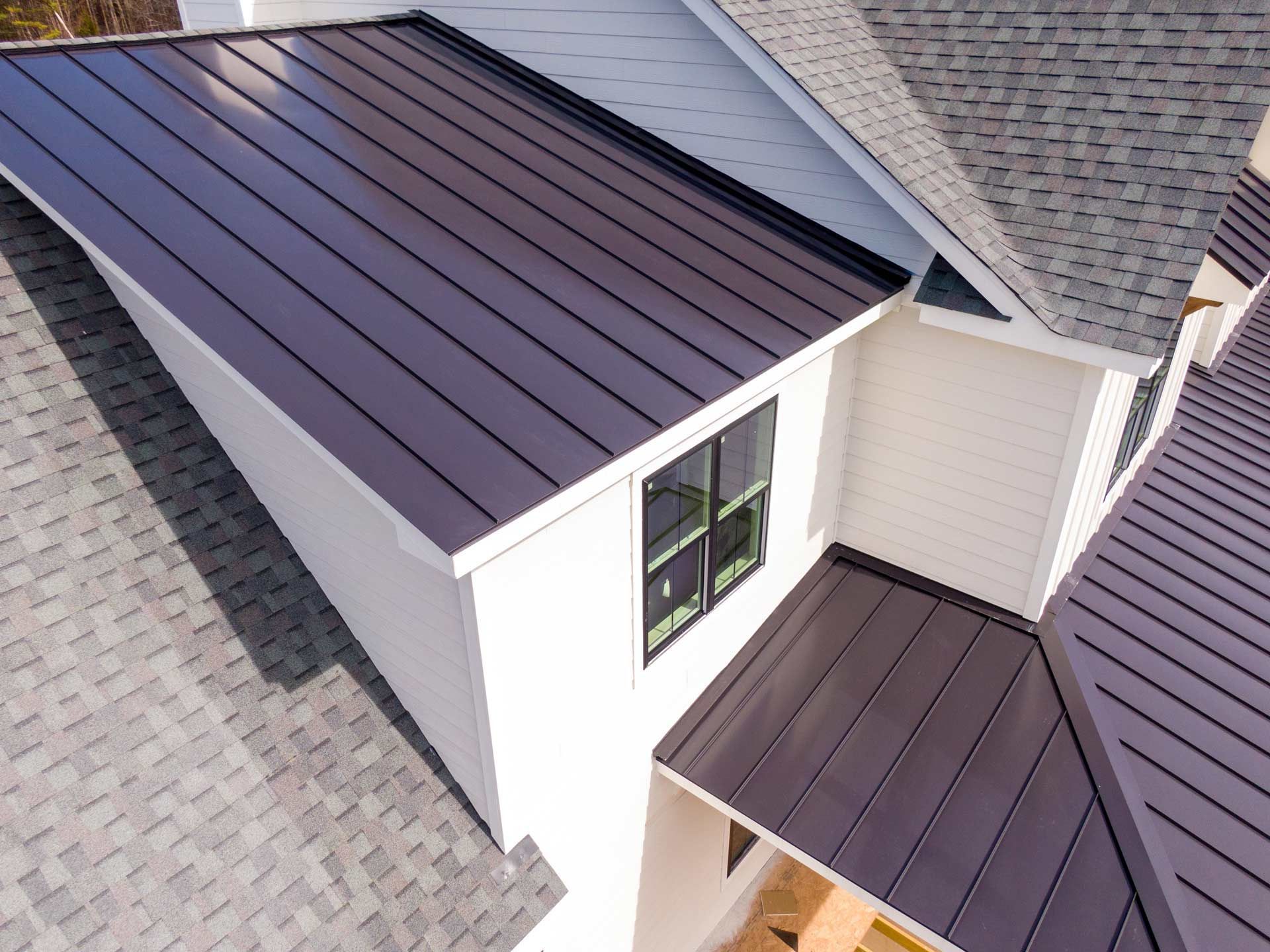 Overhead view of a house with a dark brown metal roof and white siding. Gray shingle roof adjacent.