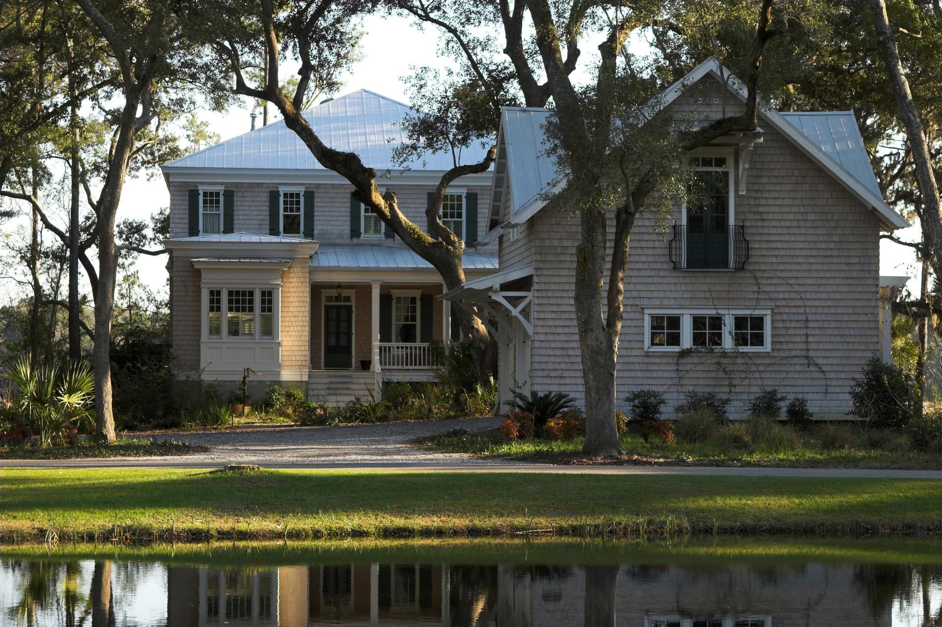 Two-story wooden house with a connecting structure. Trees surround the building, with a pond reflecting the scene.