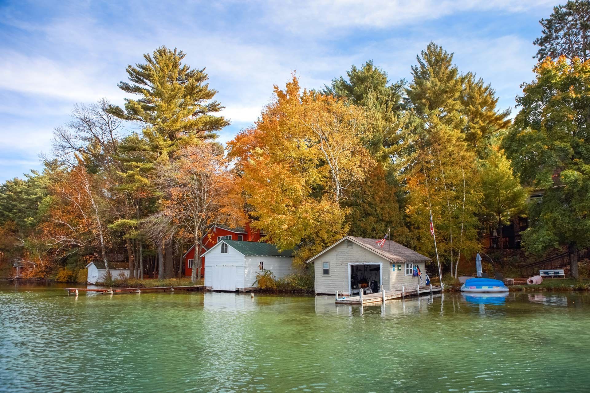 Boathouses on a lake with trees in fall colors reflected in the water.