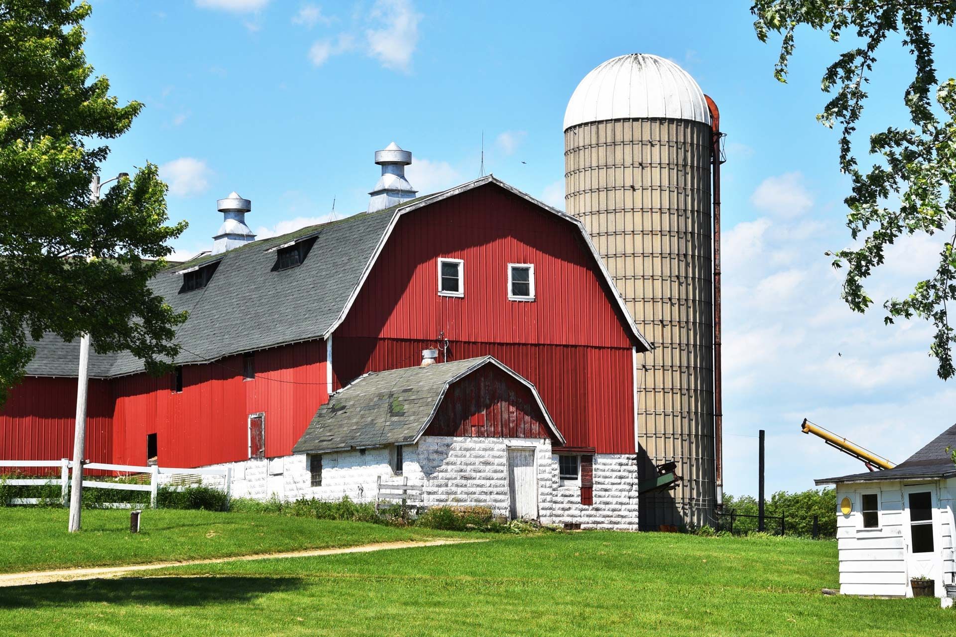 Red barn and silo on green grassy field, under a blue sky.