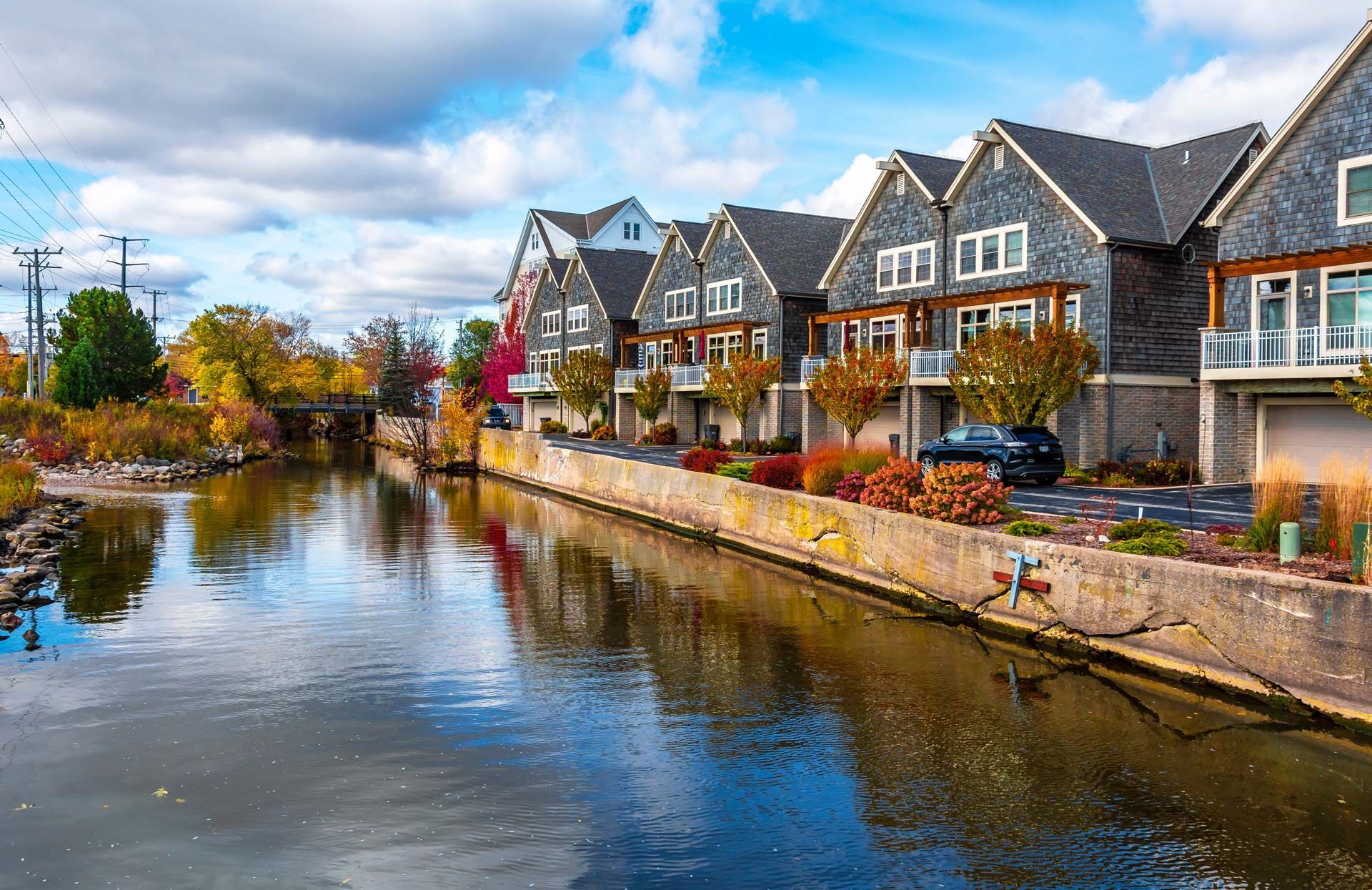 Row of houses along a canal with reflections. Fall colors, blue sky.
