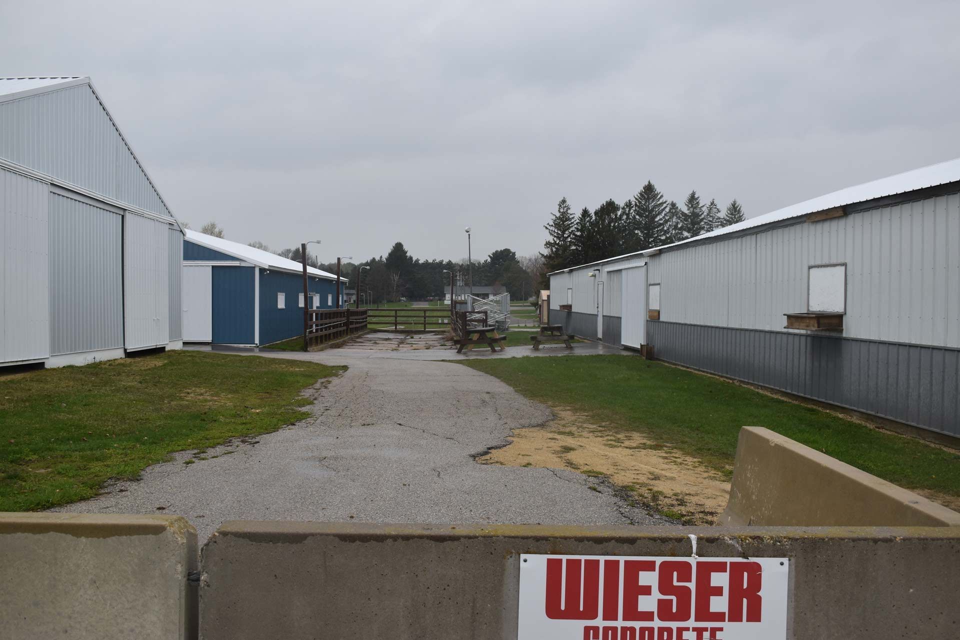 Gravel path between white farm buildings, overcast sky. 