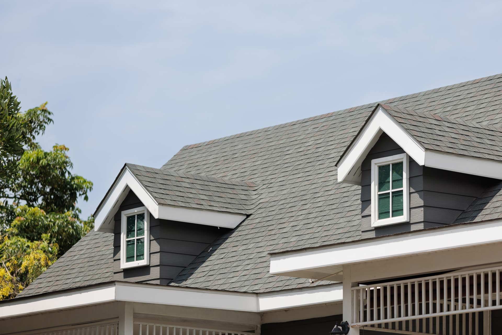 Gray roof of a house with dormer windows, blue sky in the background.
