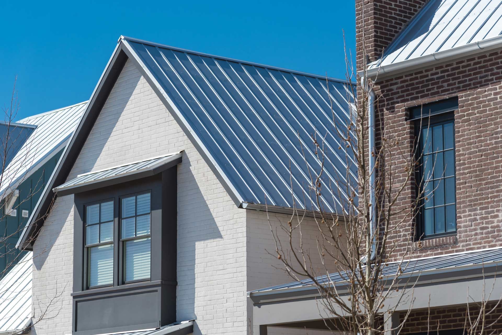 White brick house with gray roof, black framed window, and blue sky.