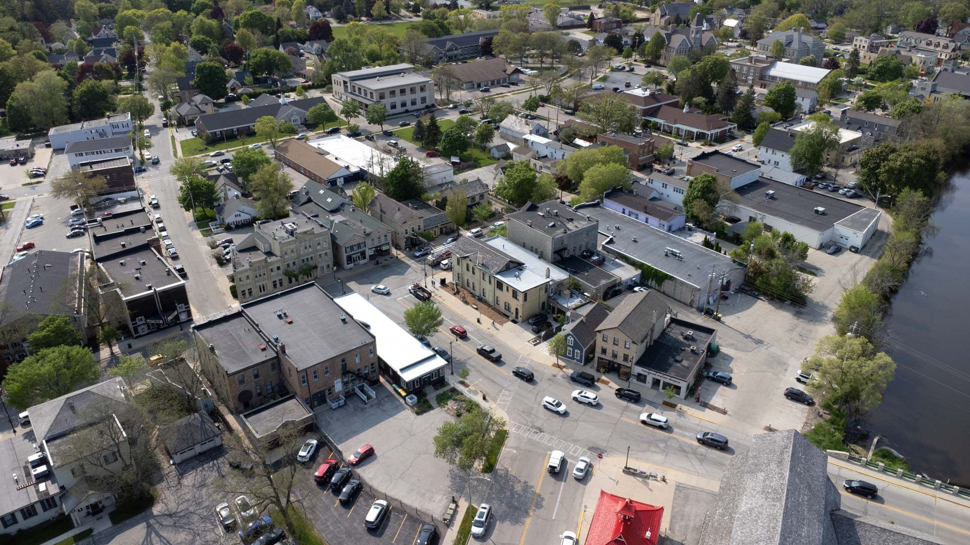 Aerial view of a town with buildings, streets, and cars; trees and a river visible.