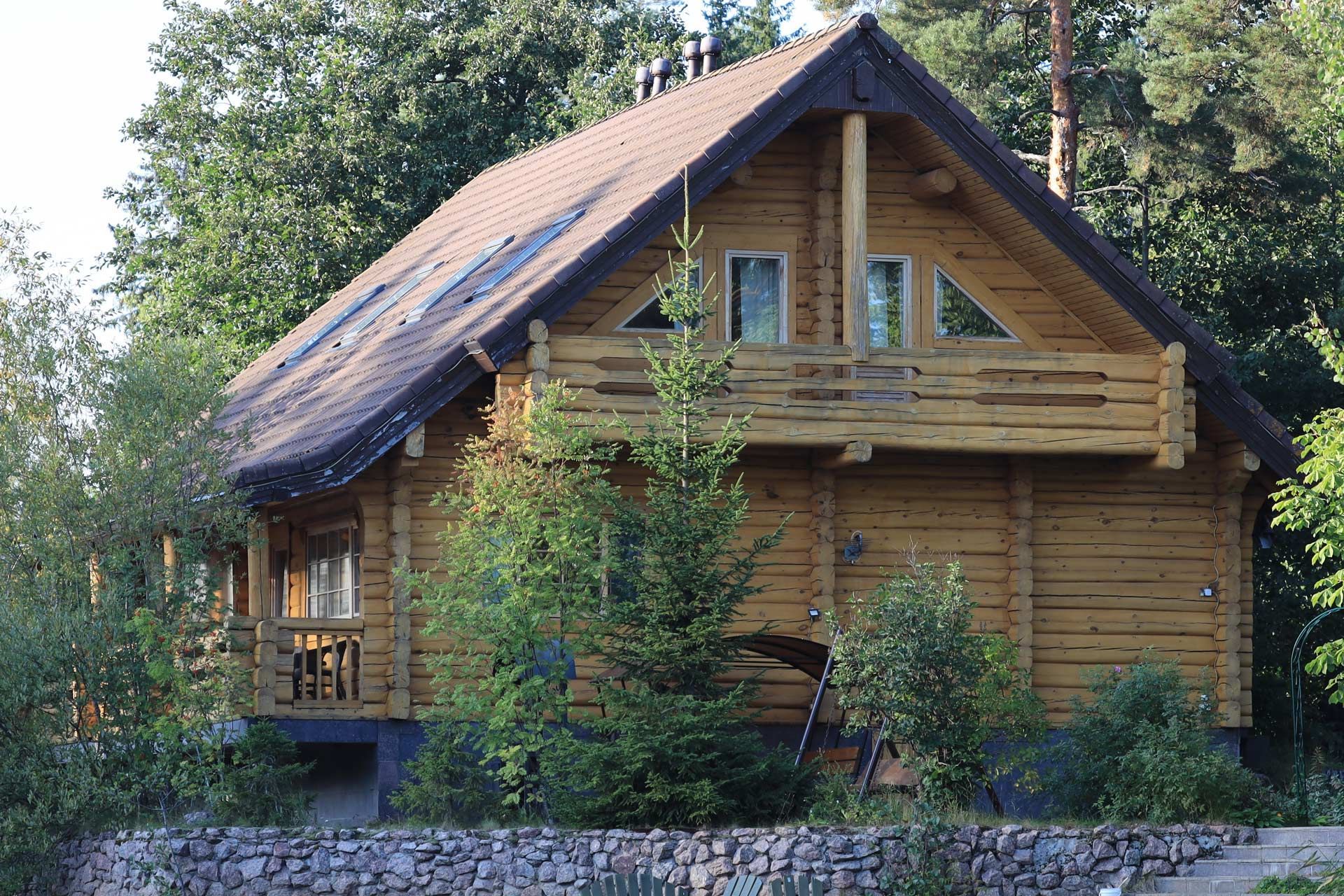 Wooden cabin with balcony and gabled roof, nestled among trees.