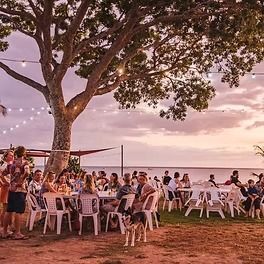 People dining outdoors under a large tree, near a beach at sunset — Darwin Catering Company in Brinkin, NT